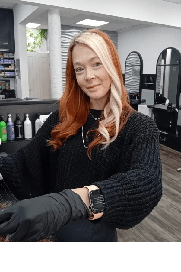 Candice, Advanced Senior Stylist at Hair Pro UK in Bexhill-on-Sea, smiling confidently in front of the salon’s branded backdrop, representing years of professional experience, colour mastery, and specialist hair extension expertise.