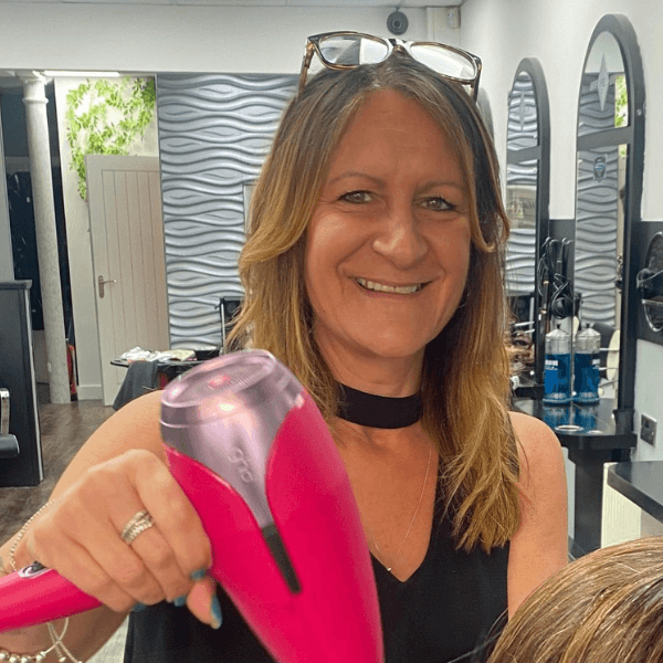 Sam, the salon owner of Hair Pro UK in Bexhill-on-Sea, smiling warmly in front of the salon’s branded backdrop, representing over 30 years of professional hairdressing expertise and premium client care.